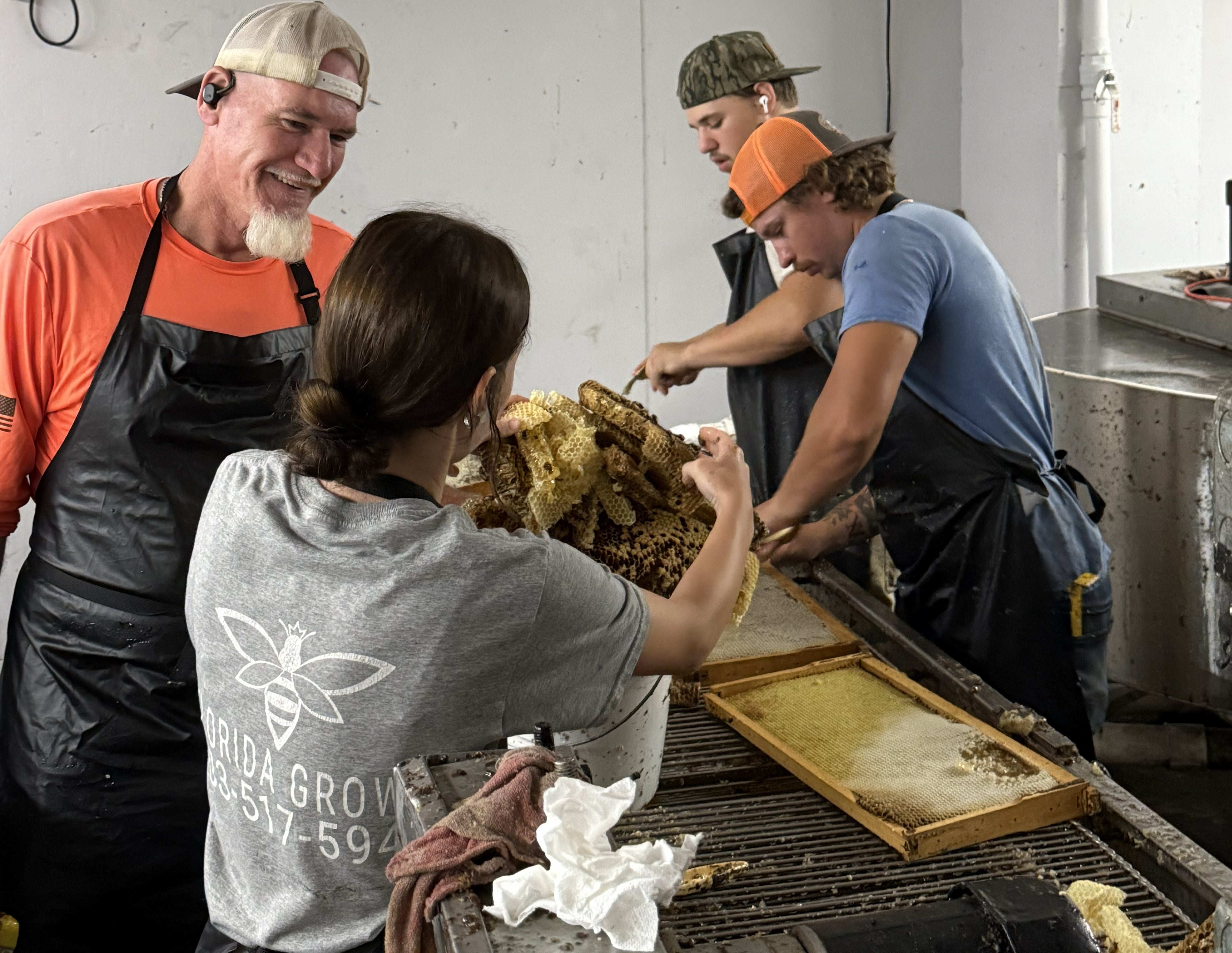 A Florida beekeeper in protective gear examines a wooden hive, showcasing hands-on apiary management.
